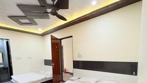 A hotel room with two beds, a ceiling fan, and a door leading to a bathroom. - Hotel Shyam Mahal (Khatoo)