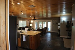 A kitchen with a wooden ceiling, granite countertop, stainless steel refrigerator, and a dining area with a chair and table. - ISLAND LAKE ESCAPE
3-bedroom house on spring fed Island Lake in Fort McCoy (Fort McCoy)