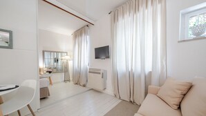 Ein modernes Hotelzimmer mit Sofa, Essbereich, Fernseher und großem Fenster mit Vorhängen.