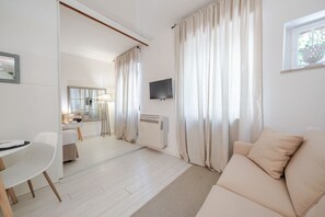 Ein modernes Hotelzimmer mit Sofa, Essbereich, Fernseher und großem Fenster mit Vorhängen.