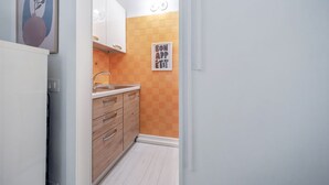 Eine schmale Küche mit Holdekor-Schränken, einer weißen Arbeitsplatte und einer gefliesten Rückwand.