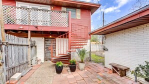 Eine rote Treppe führt zu einem Balkon, einem Holzzaun und einer Pflasterterrasse mit Blumentöpfen.