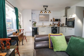 A compact living space with a kitchenette, a dining area, and a sofa with cushions. - Shell Cottage (Bournemouth)