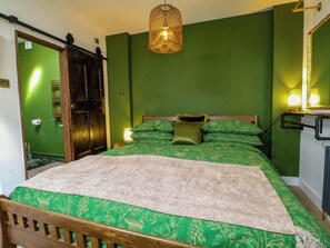 A room with a bed, green walls, a wooden door, a hanging light fixture, and a mirror. - Shell Cottage (Bournemouth)