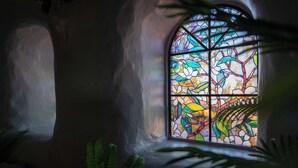 Una vidriera con motivos florales, una pared de piedra y follaje verde.