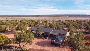Una casa con un espacio exterior techado, rodeada de árboles y un paisaje abierto y extenso.