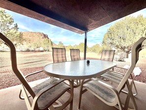 Een overdekt terras met een ronde tafel en comfortabele stoelen, met uitzicht op een mooi landschap met bomen en heuvels.