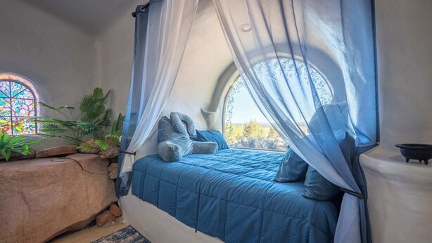 Un dormitorio con cama de dosel, pared de piedra, ventanal con vidrieras y vistas al exterior.