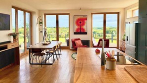 A modern kitchen with a large island, dining area with chairs, and a view of the countryside. - Grand Chapel with Views in Peaceful Devon Hills (Devon)
