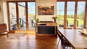 A spacious room with a large wooden table, a radiator, and a view of a garden and building through large sliding doors. - Grand Chapel with Views in Peaceful Devon Hills (Devon)
