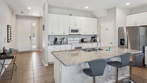 Una cocina moderna con gabinetes blancos, encimera de granito, electrodomésticos de acero inoxidable y una zona de bar con taburetes.