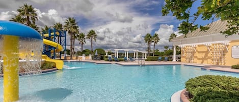 A swimming pool with a water slide, palm trees, and a covered seating area.