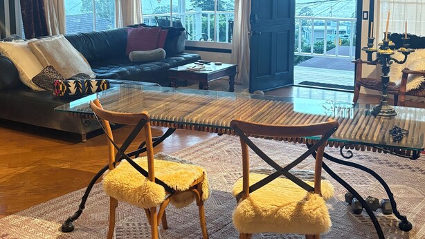 Un salon comprenant un canapé, deux fauteuils, une table basse en verre, un ventilateur de plafond et une vue dégagée grâce à de grandes fenêtres.