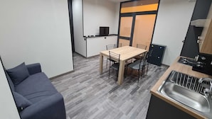 Un angolo cottura compatto con lavello, un piccolo tavolo da pranzo con sedie, un divano e una TV a parete.