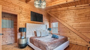 Ein Schlafzimmer einer Holzhütte mit einem großen Bett, zwei Nachttischen, einer Pendelleuchte und einem Fenster.