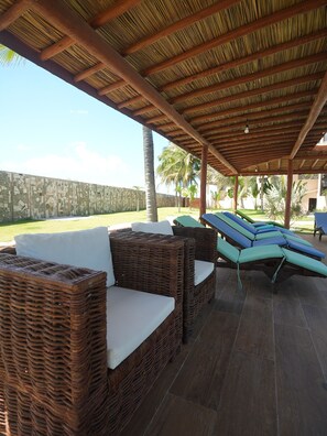 A covered outdoor seating area with wicker furniture and cushions.