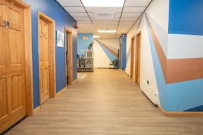 A hotel hallway with wooden doors, blue walls, and a geometric mural.