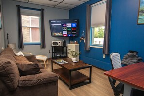 A living room with a brown couch, a wooden coffee table, a flat-screen TV mounted on the wall, and a window with curtains. - Two-Room Suite, 1.6 - First Floor (Malone)