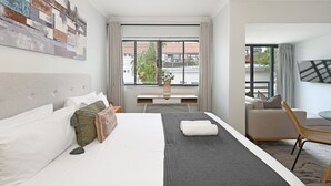 A hotel room with a bed, a desk, a chair, and a TV. - Sea Point Studio | Pool | Gym | BBQ (Cape Town)