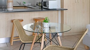 A modern kitchen with a glass-top table, wicker chairs, a microwave, and a potted plant. - Sea Point Studio | Pool | Gym | BBQ (Cape Town)
