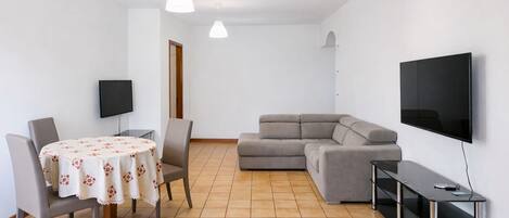 A modern living room with a dining table, two chairs, a sofa, a TV, and a TV stand.