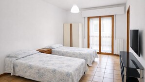 A bedroom with two beds, a TV, a wardrobe, and a sliding glass door. - Modern apartment in center with beach included - Alba Adriatica (Alba Adriatica)