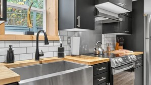 Een moderne keuken met een roestvrijstalen spoelbak, zwarte kastjes, een houten aanrechtblad en een ingebouwde kookplaat.