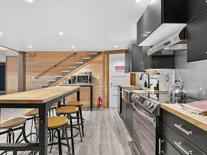 A modern kitchen with a wooden staircase, a dining area with stools, and a kitchen island. - LifeSize Dinos 4BR HotTub (Washougal)