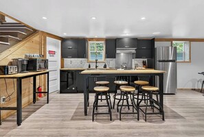 A modern kitchen with a central island, bar stools, a stainless steel refrigerator, and a staircase. - LifeSize Dinos 4BR HotTub (Washougal)