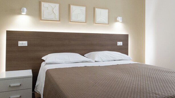 Een opgemaakt bed met een bruine sprei, een houten hoofdbord en drie wandlampen.