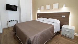 Een keurig ingerichte hotelkamer met een groot bed, een nachtkastje met lades, een flatscreen televisie aan de muur en een klein bijzettafeltje met een handdoekhouder.