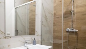 Een badkamer met een wit wastafel, een spiegel en een douche met glazen wanden.