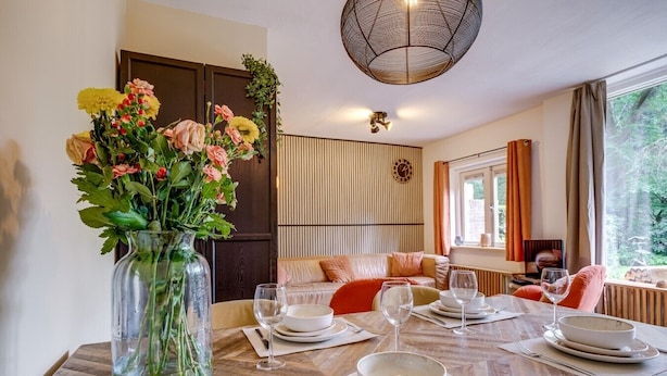 Een eetgedeelte met een houten tafel voor vier personen, een bloevas en uitzicht op een tuin door een raam.