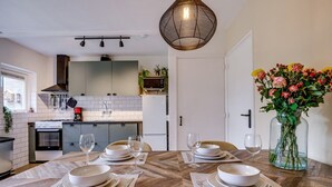 Een moderne keuken met witte kasten, een inbouwoven en een eethoek met witte borden en glazen.