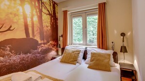 Een slaapkamer met een bed, twee nachtkastjes, een raam met gordijnen, een muurschildering en een lamp.