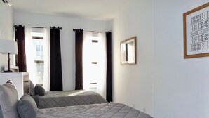 A room with two beds, a desk, a chair, and a window with curtains.