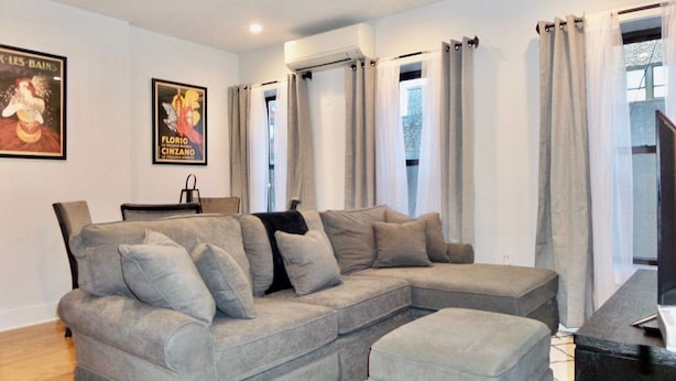 A living room with a grey sectional sofa, a flat-screen TV, and a poster on the wall.