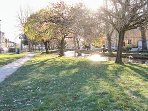 A park with a stone bridge over a canal, surrounded by trees and a pathway. - Meadow Lodge (Cirencester)