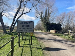 A sign for Cerney Wick, Saxon Parish, Charter AD999, with a rural road and trees. - Meadow Lodge (Cirencester)