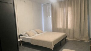 A single bed with a beige blanket, a bedside table, a chair, and a wardrobe in a room with a grey floor and white walls. - Cozy room for 4 · Shared bathroom · Peaceful area (Březová)