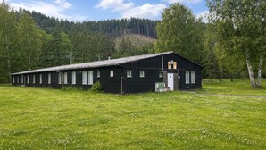 A black wooden building with a white door and windows, surrounded by a grassy field and trees. - Cozy room for 4 · Shared bathroom · Peaceful area (Březová)