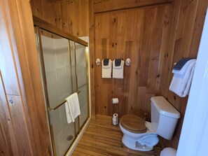 Une salle de bain aux murs lambrissés, dotée d’une douche en verre, de toilettes et d’un porte-serviettes.