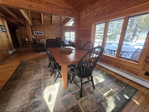 Un intérieur en bois avec une table et des chaises, de grandes fenêtres et une cheminée.