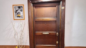 Una porta di legno con una maniglia, un tappetino d'ingresso con un bicchiere da vino e del testo, e un vaso con girasoli.