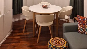 Zona pranzo moderna con tavolo rotondo, due sedie, una lampada a sospensione rossa, un armadietto bianco e un pouf decorato.