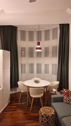 A modern dining area with a round table, two chairs, a red pendant light, a white cabinet, and a patterned ottoman. - A Window on Garbatella (Roma)