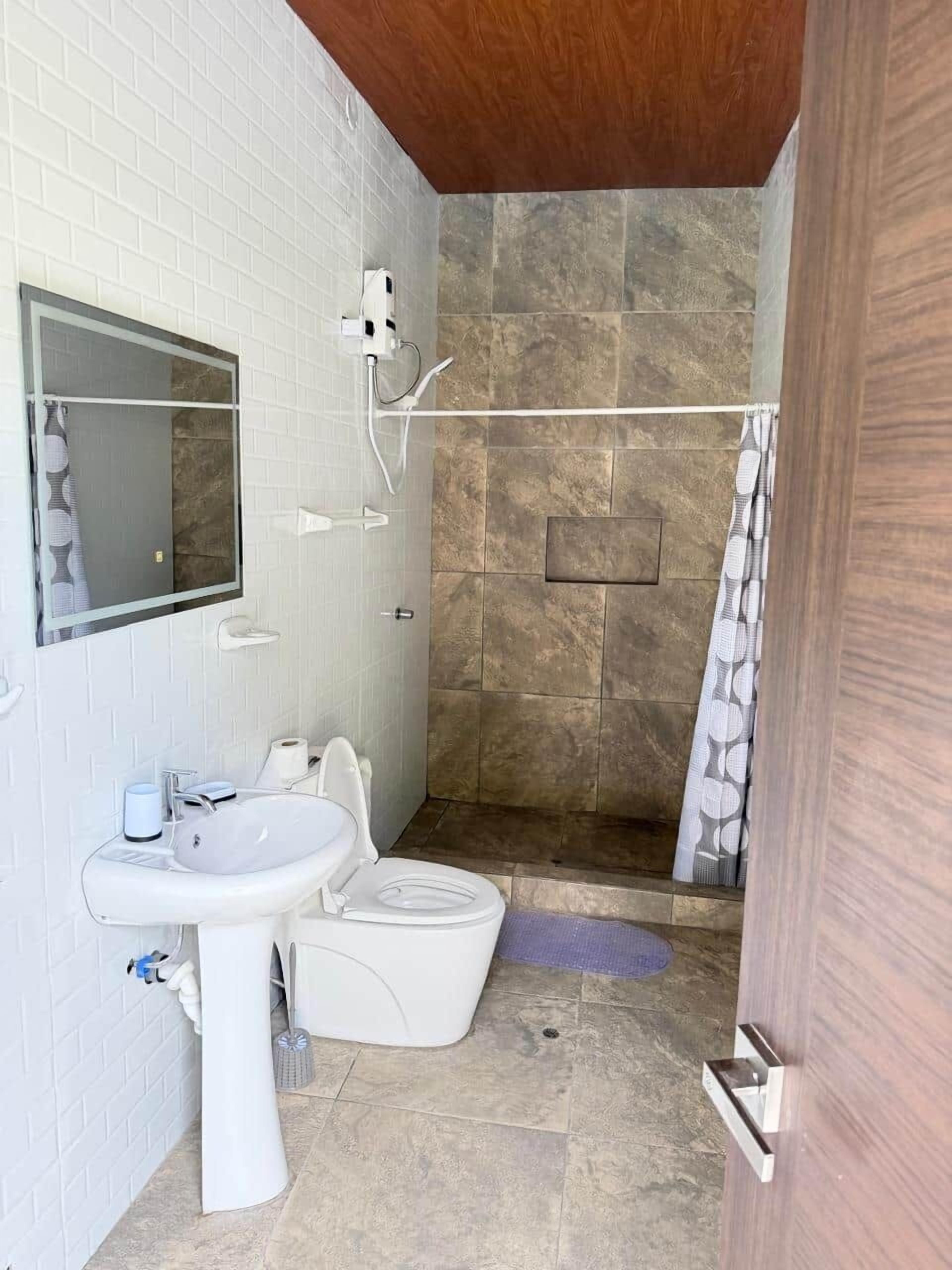 Un baño con lavamanos blanco, espejo, ducha y techo de madera.