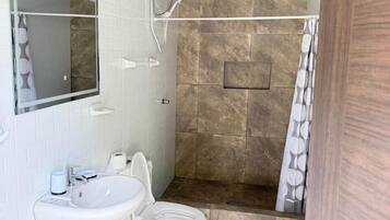 Un baño con lavamanos blanco, espejo, ducha y techo de madera.
