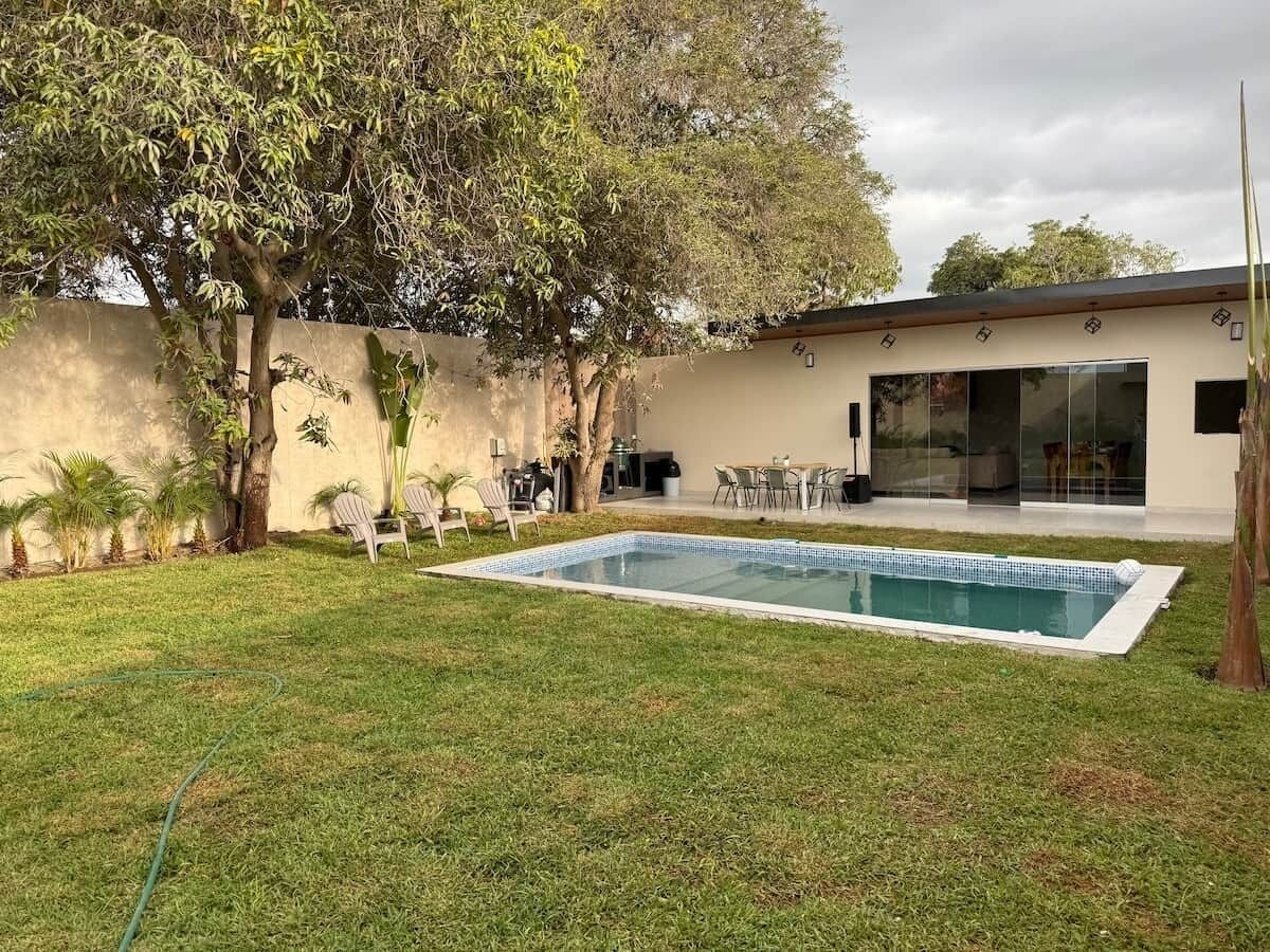 Un patio trasero con piscina, un porche con sillas y un edificio con grandes ventanales.
