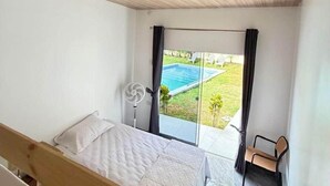 A bedroom with a wooden ceiling, a bed, a chair, a fan, and a view of a swimming pool through a glass door. - Casa en Ica con piscina, parrilla y gran jardín (Ica)